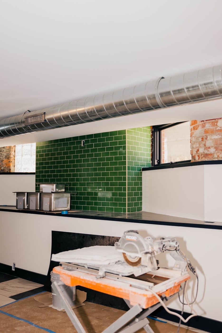 Green-tile bar wall mid buildout with a tile saw and brick around the windows