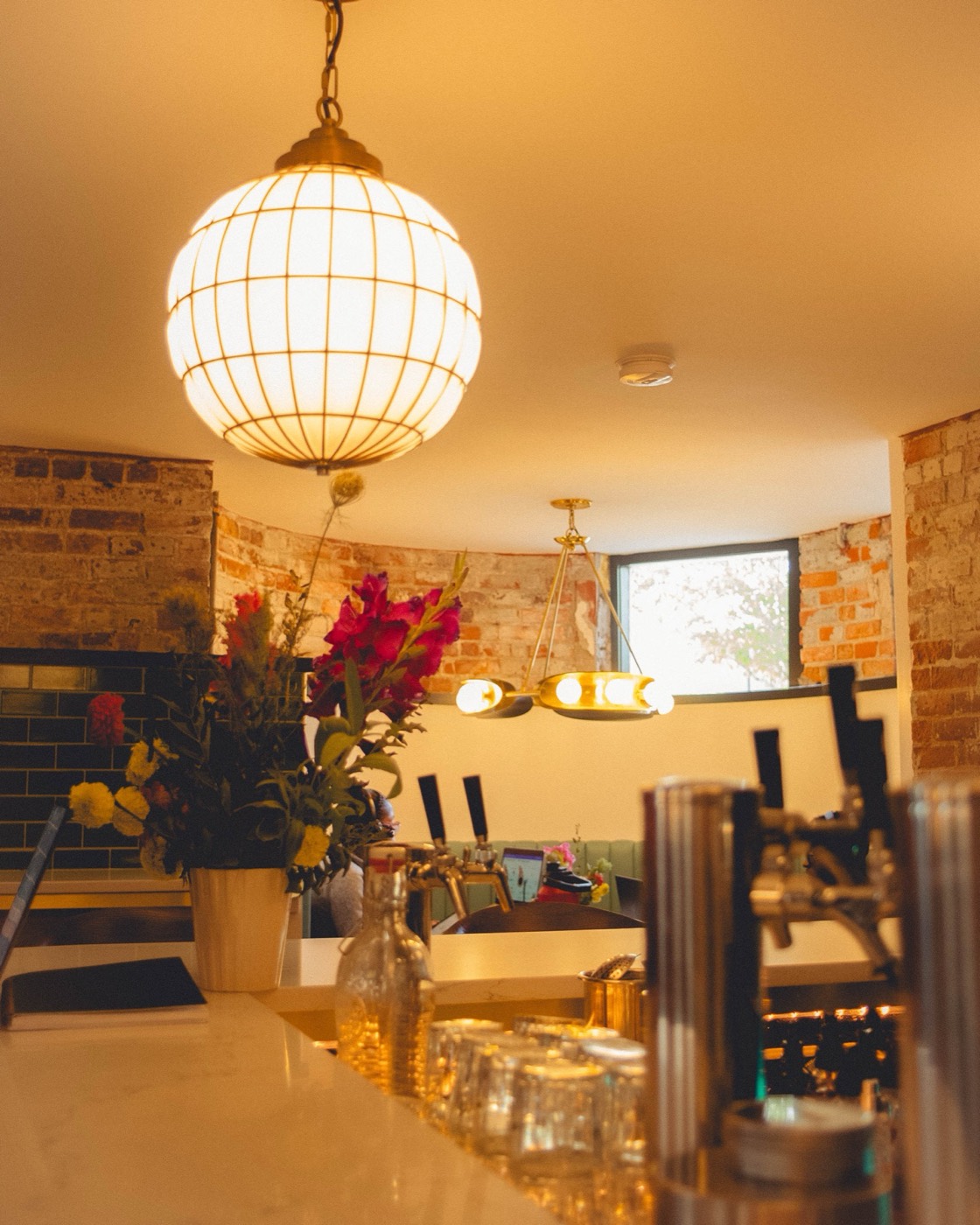 Cafe Sous Terre interior, bar with brass pendant light, draft taps, and flowers