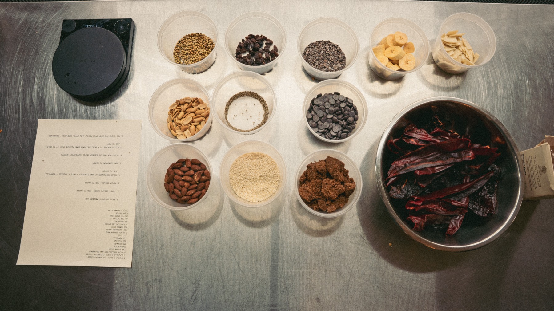 Recipe development: ingredients portioned on a steel bench with a scale and a written recipe