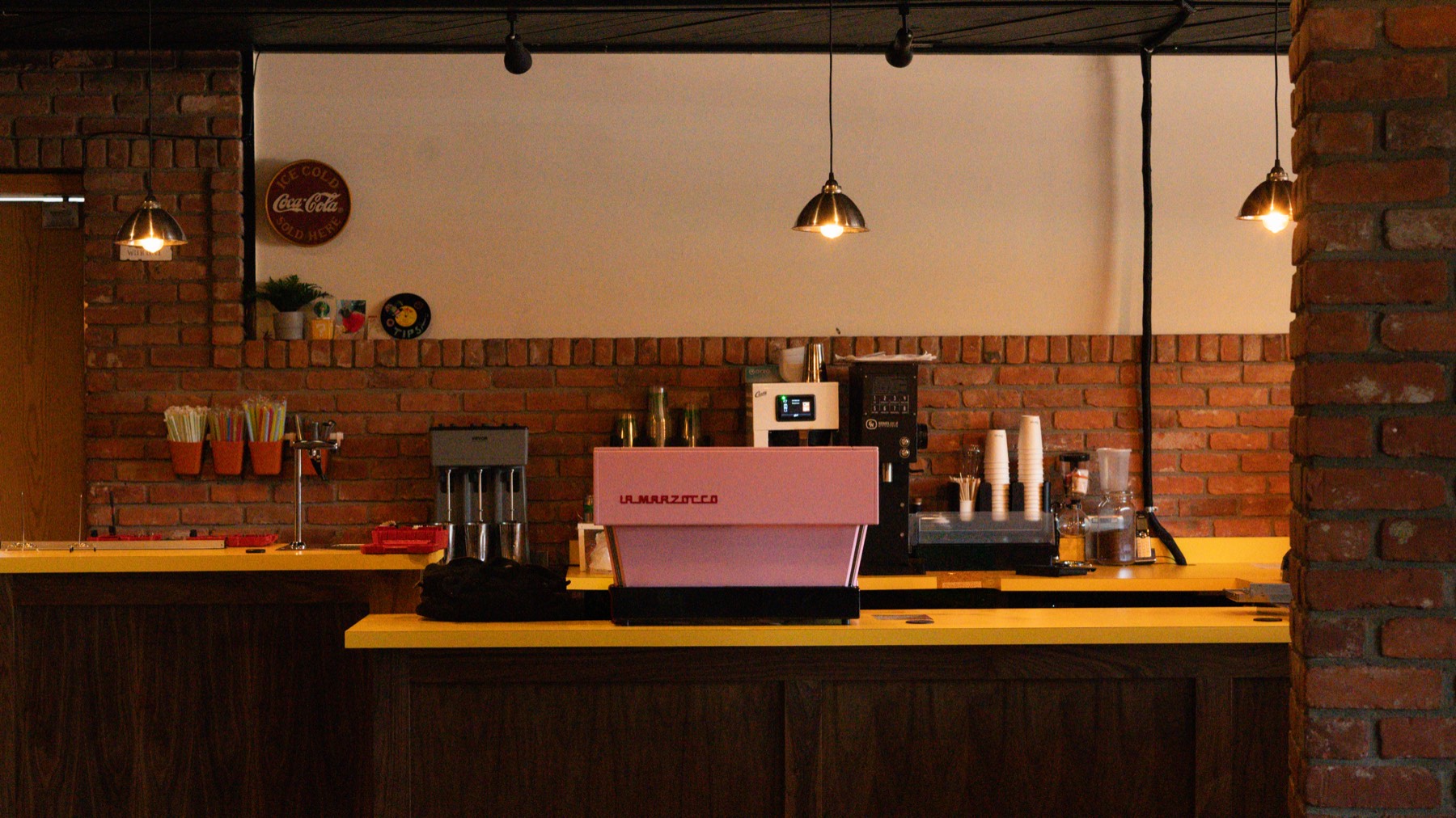 Pink La Marzocco espresso machine on a yellow bar with brick walls and pendant lights