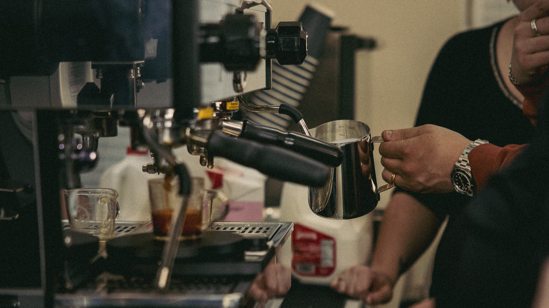 Hands steaming milk on an espresso machine during a class
