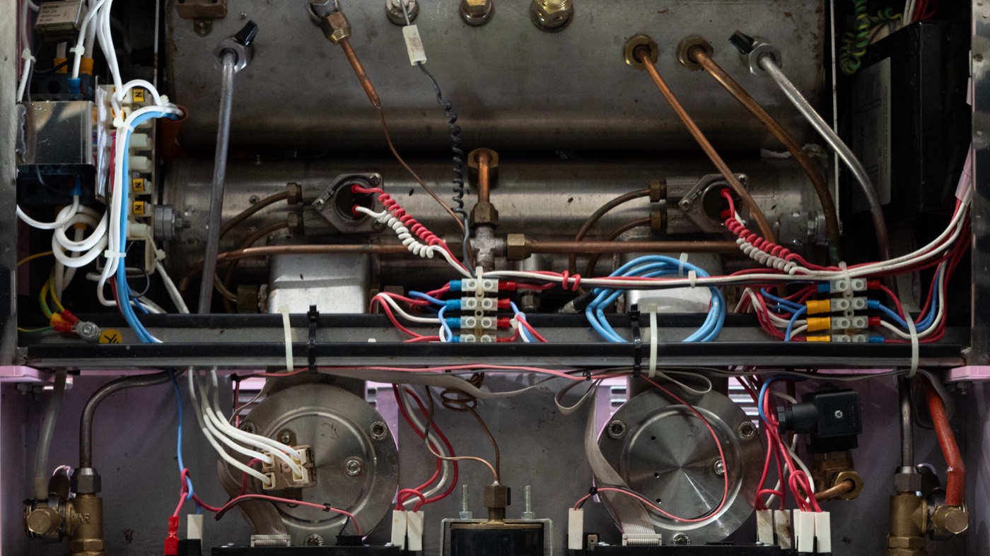 Inside an espresso machine, boiler, copper plumbing, and wiring exposed